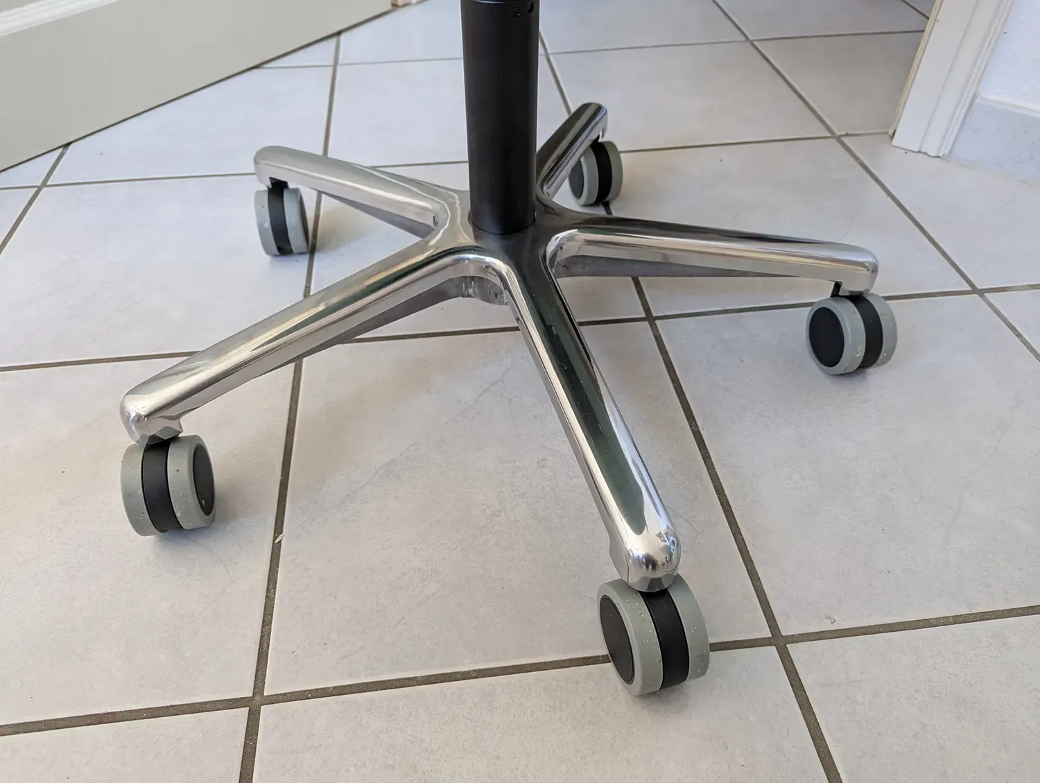 Aluminium-Fußkreuz mit fünf Rollen und schwarzer Stuhlsäule auf einem Fliesenboden