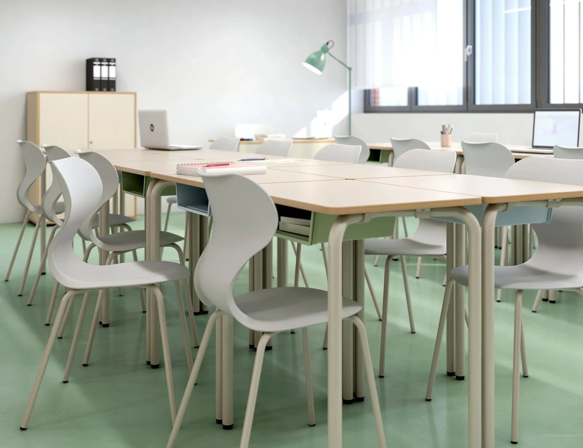 Rechteckige Schülertische und grüne Stühle in einem hellen Klassenraum