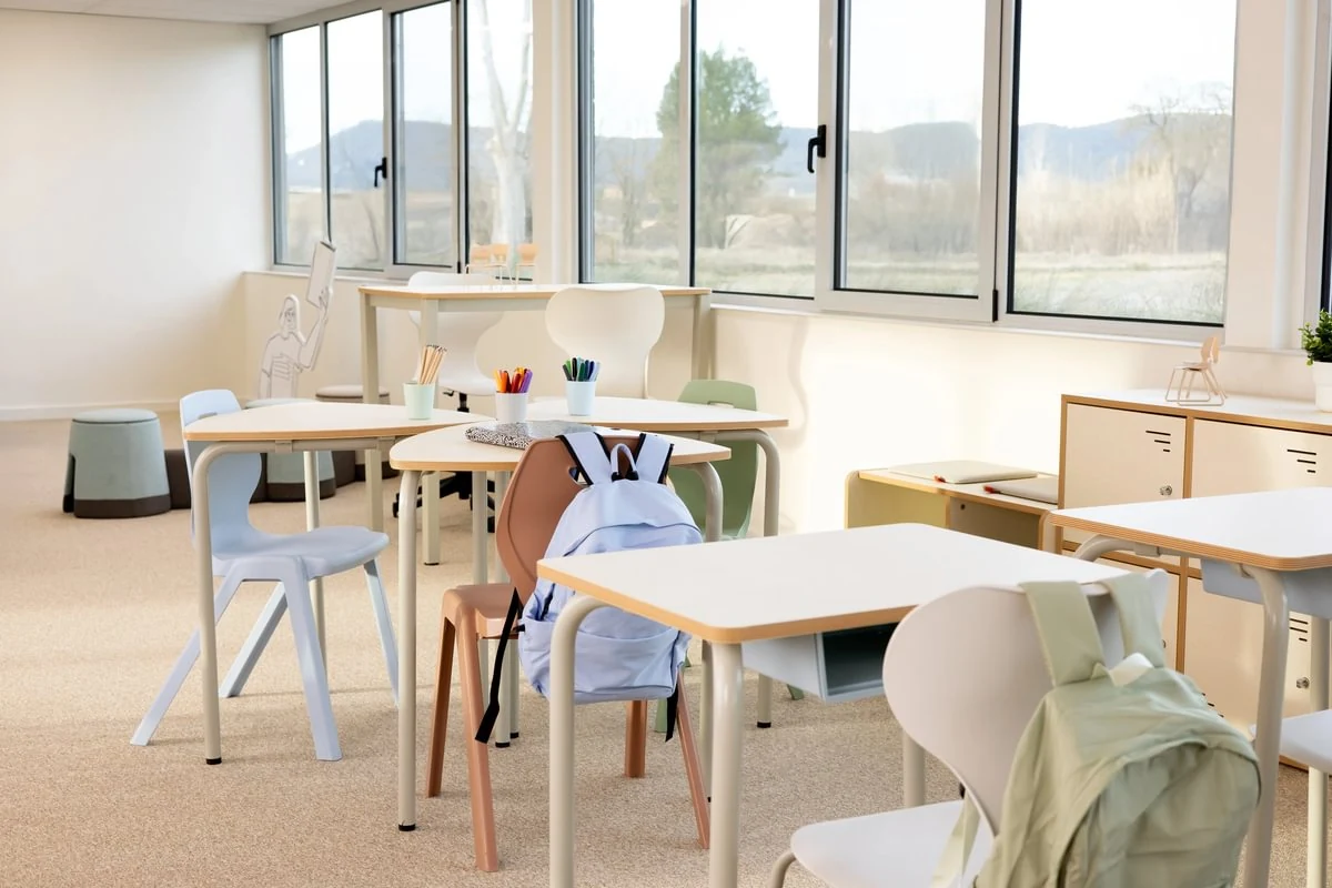 Heller Klassenraum mit pastellfarbenen Schulstühlen, einzelnen Schultischen und niedrigen Aufbewahrungsmöbeln
